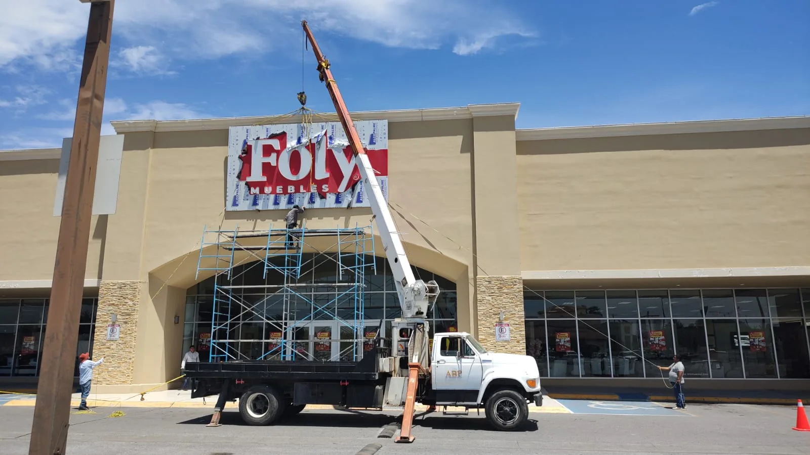 Montaje del anuncio luminoso de Foly Muebles sobre la fachada, con grúa titán y andamio
