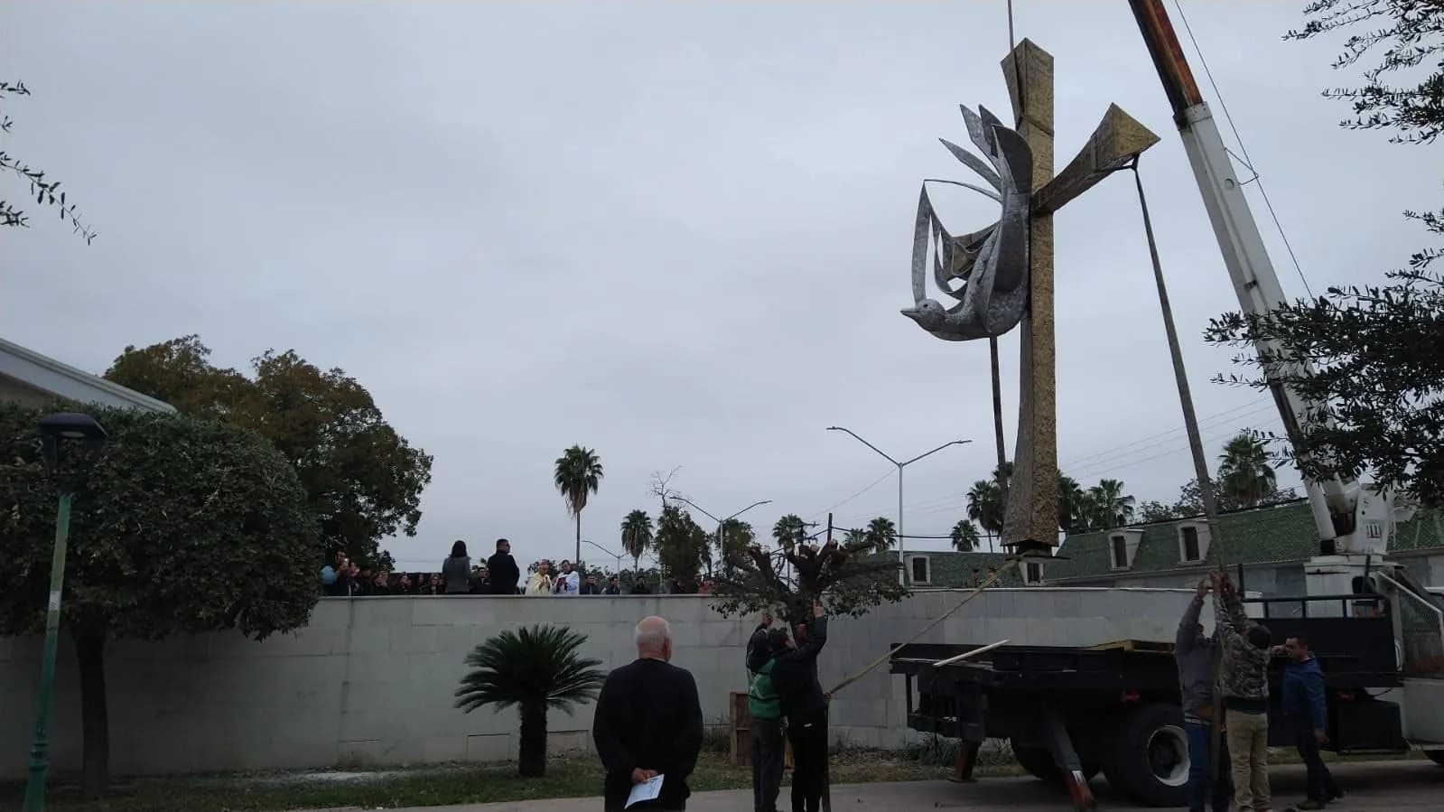 Colocación de una cruz de acero con paloma en el atrio de una iglesia, con la comunidad presente